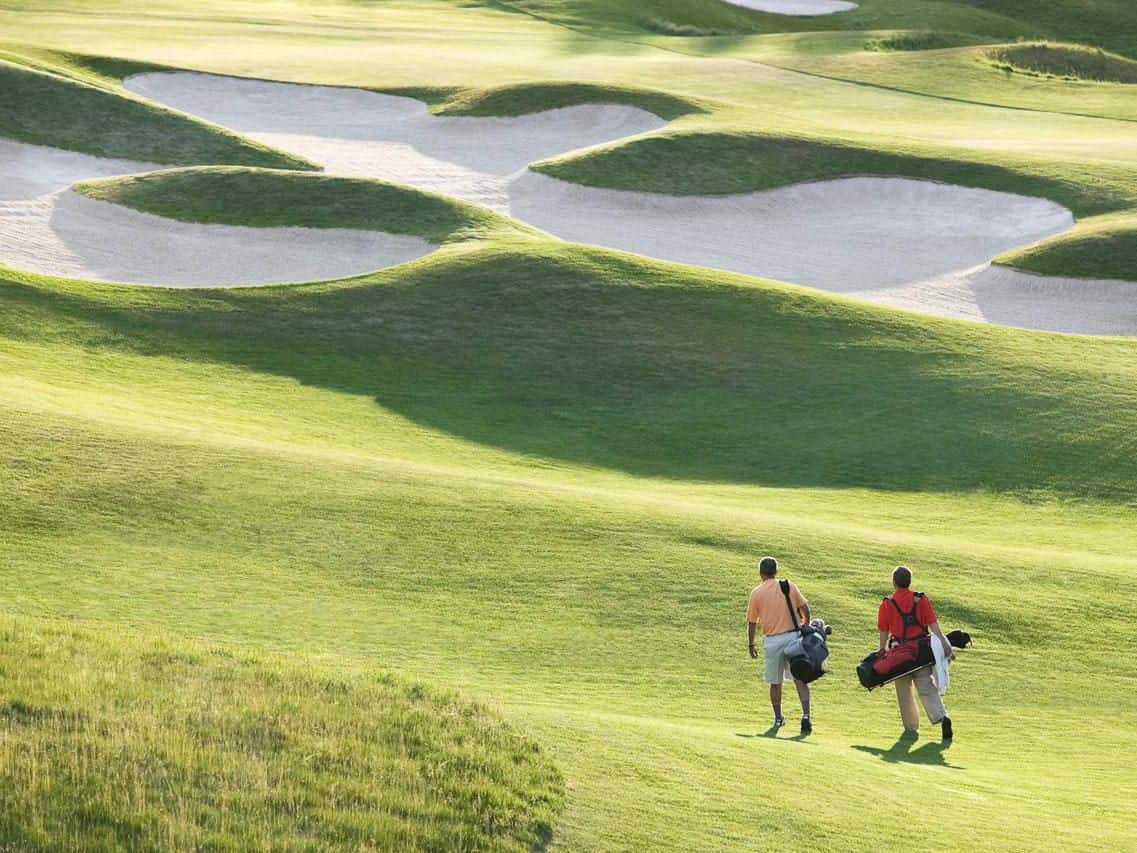 Two men walking across golf course next to sand bunkers holding their clubs