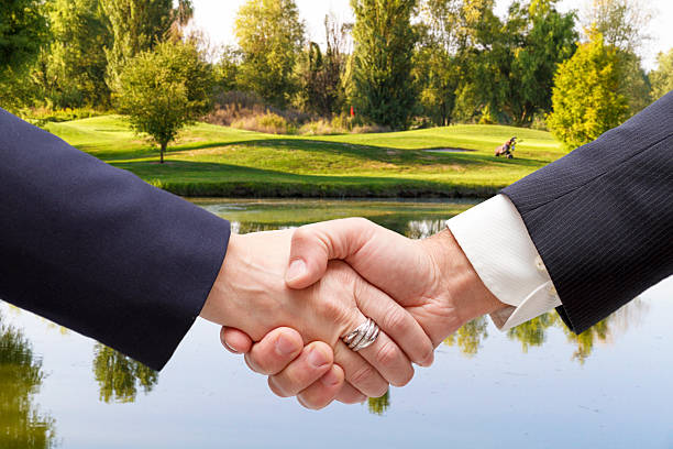 Businessmen handshaking with golf course in the background